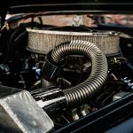 Detailed view of vintage car engine with open hood on a sunny day.