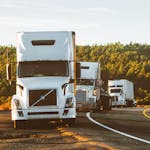 Three semi trucks driving on a highway through a forested landscape in Arizona.