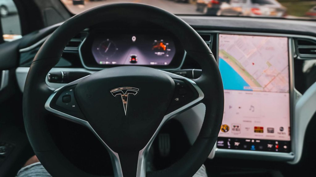 Interior view of a Tesla Model X steering through palm-lined streets of Santa Monica at twilight.