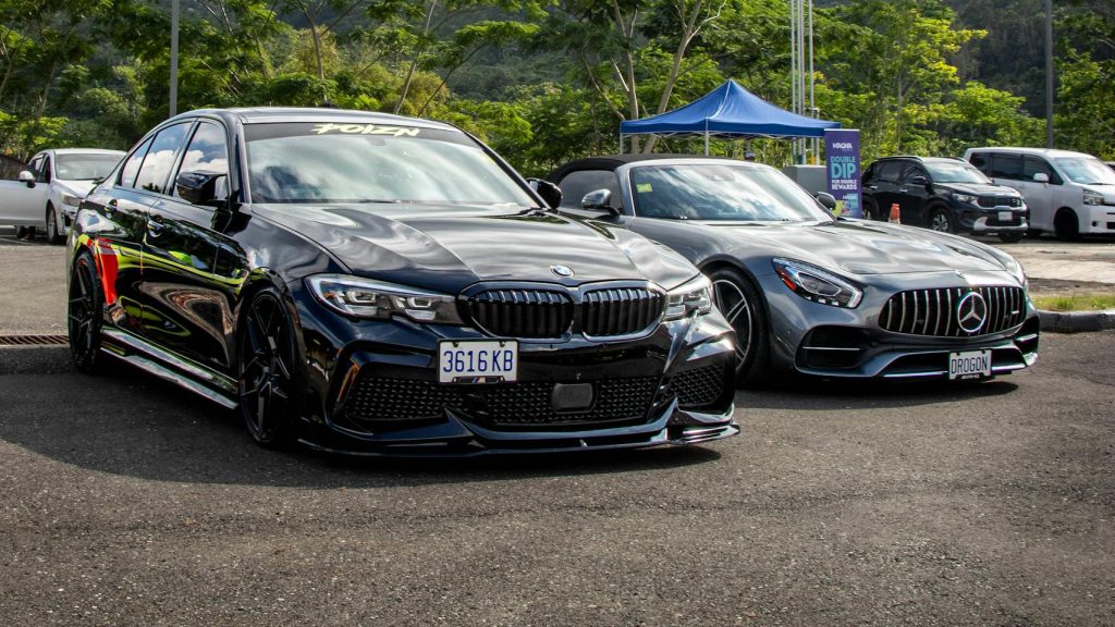 Two luxury cars parked outdoors with a lush Jamaican backdrop.